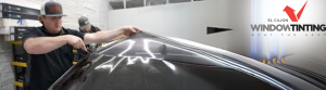 Two technicians at El Cajon Window Tinting apply a large sheet of window film to a vehicle roof with precision, inside a professional workspace. The company’s logo and slogan “Beat the Heat” are displayed on the wall in the background.