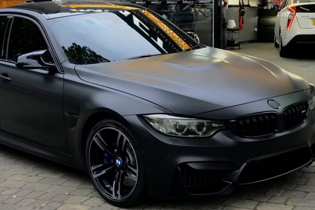 Matte black BMW with a full vinyl wrap parked outside an automotive shop.