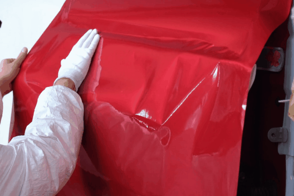 Technician applying a glossy red vinyl wrap over a vehicle body panel during professional car wrap installation.