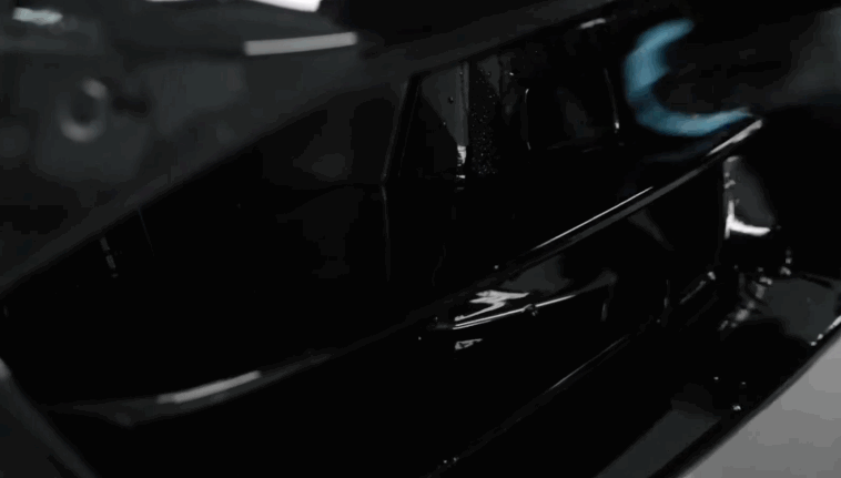 Close up of a dark vehicle grille with water droplets beading tightly on the surface after ceramic coating treatment. The hydrophobic effect shows strong water repellency.