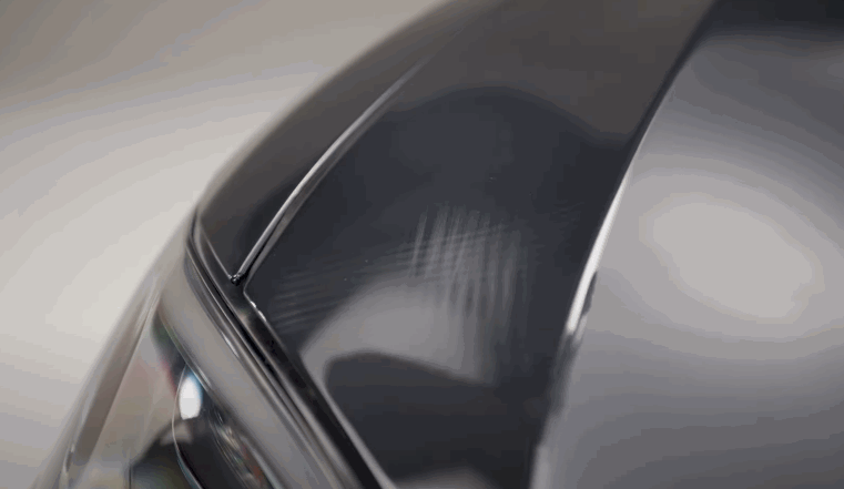 Close up of a glossy black car hood showing smooth reflections and a sharp panel edge after paint correction removes imperfections. The finish appears mirror like under soft lighting in a controlled indoor setting.