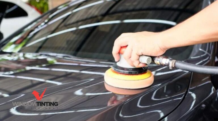A technician using a machine polisher on a dark colored car panel to refine the surface during paint correction. The spinning pad works across the paint to remove swirl marks and enhance shine while a logo reading "EL CAJON WINDOW TINT" appears in the corner.