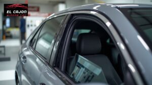Gray sedan with newly installed window tint on the side windows parked inside a shop, with the logo "EL CAJON WINDOW TINT" visible in the top left corner. The slightly lowered window shows the clean edge and professional finish of the tint.