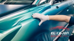 Technician applying a teal vinyl wrap to a car at El Cajon Window Tinting in El Cajon, CA.